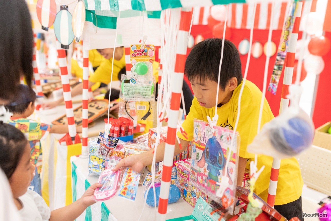 こども縁日・こども店長体験子どもたちが縁日の店長となって接客やサービス提供を行う、こども万博の象徴的なコンテンツです。射的、ヨーヨー釣り、千本くじなどの縁日を子どもたち自身が運営します。大人が用意した体験をするのではなく、子ども自身が主体的に行動し、困りごとを周りと協力して解決する力を養います。ストライプ柄の屋台やサーカスをイメージした装飾で、会場を明るい雰囲気に彩ります。