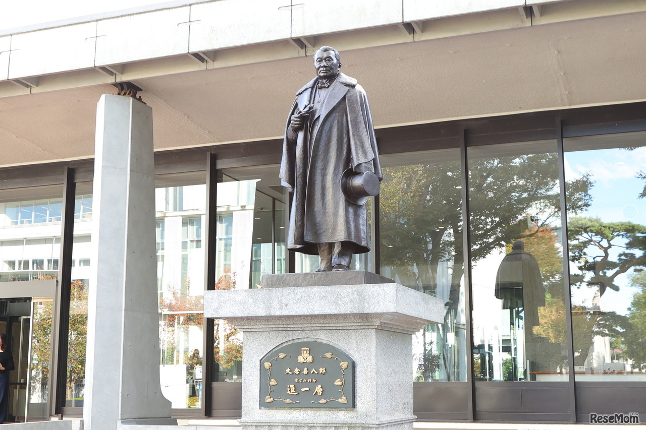 東京経済大学「大倉喜八郎 進一層館」前の銅像。東京経済大学は、1900（明治33）年、明治・大正期の実業界の雄である大倉喜八郎により、 当時の赤坂葵町（現在の東京・虎ノ門「オークラ東京」隣接地）に創立された大倉商業学校を前身としている。大倉喜八郎が設立し経営に腕を振るった企業は多数あり、今日も大成建設、サッポロビール、帝国ホテルなどにその偉業が刻まれる