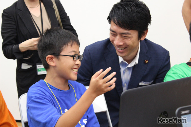 Minecraftコースの中学2年生から、Minecraftについて説明を受ける小泉氏。明確な回答と解説に「説明能力が高いね！」と驚く場面も。何かを作る楽しみや今自分が行っていることを熱心に話すようすに、小泉氏は深い感銘を受けていた